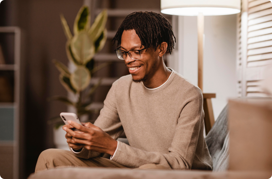 homem negro sorridente com moletom bege mexendo no celular